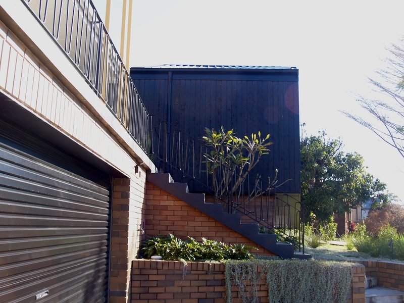 The new addition in dark cladding above the garage and brick stairs